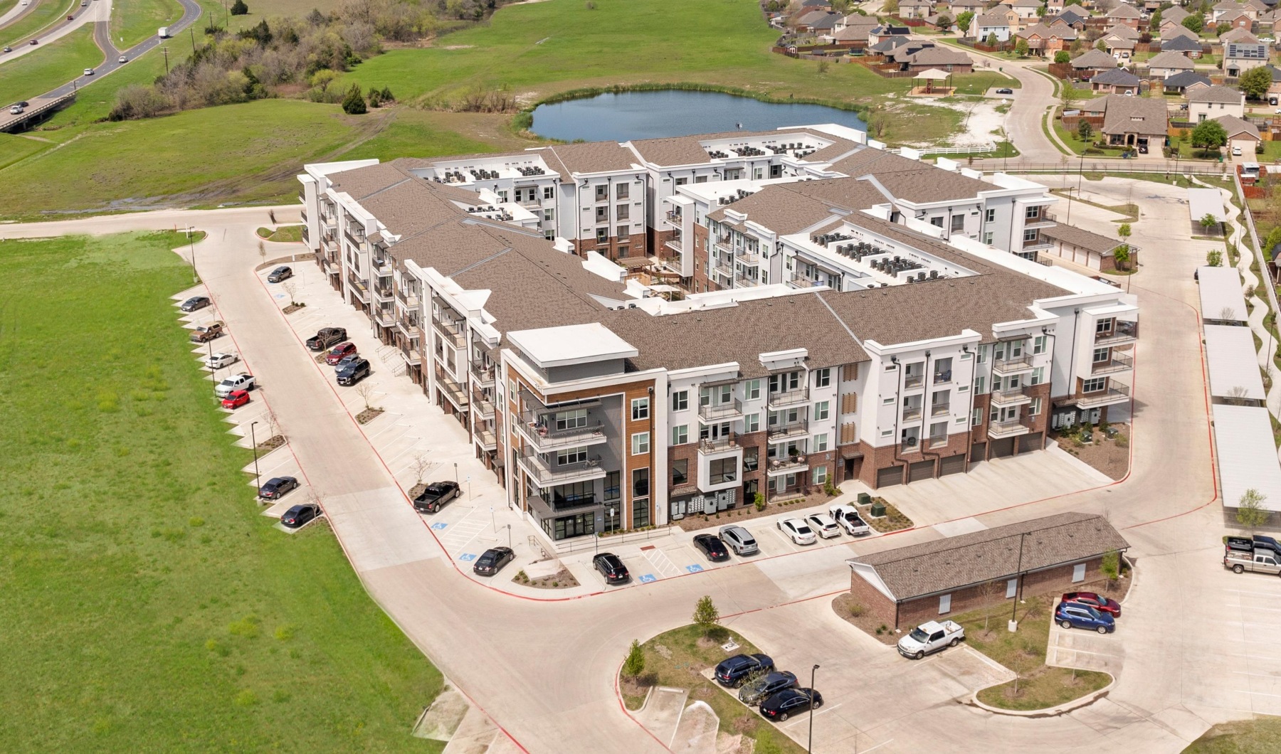 Make your apartment life exceptional Aerial view of The Village at Waxahachie with lush greenery and a pond in the back